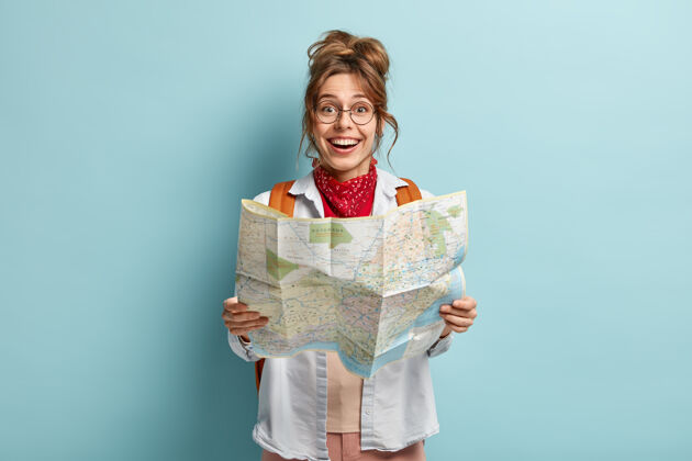眼镜快乐的女旅行者拿着地图 查看目的地的路线 在假期里穿越欧洲 背着背包 戴着圆眼镜高兴冒险指南