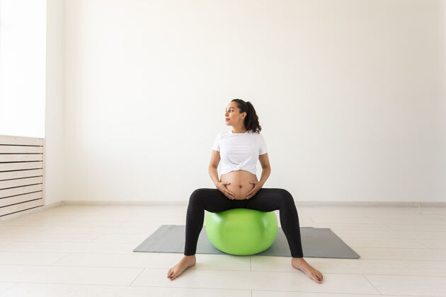 健美操一个年轻的孕妇坐在垫子上用健身球做放松运动训练腹部护理