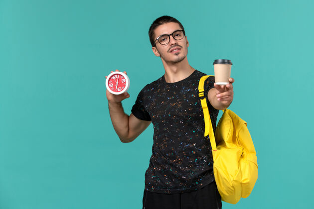 钟身穿深色t恤的男生正面图黄色背包 蓝色墙上放着咖啡和时钟前线大学黑暗